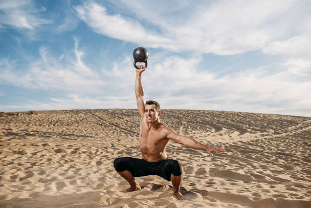 Мужчина-спортсмен делает упражнения с гирями в пустыне в солнечный день. Сильная мотивация в спорте, сильные тренировки на открытом воздухе
 - Фото, изображение