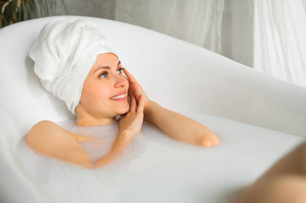 beautiful young woman with a towel on her head takes a bath with milk - Zdjęcie, obraz