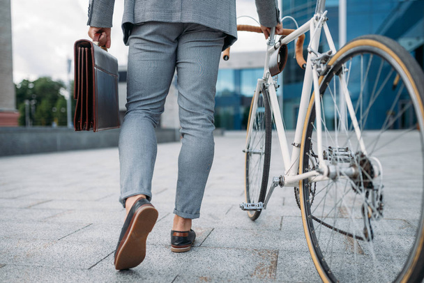 Un uomo d'affari vestito con valigetta e bici in centro. Persona d'affari a cavallo del trasporto ecologico sulla strada della città
 - Foto, immagini