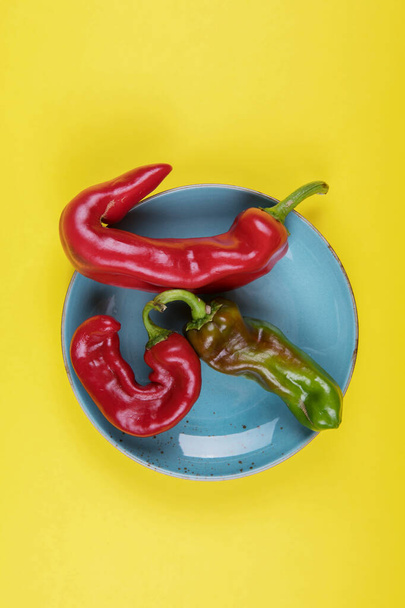 Trendy ugly red chili peppers on a blue plate on a yellow background, minimal style of nature, pop art, creative food concept, modern art - Photo, Image