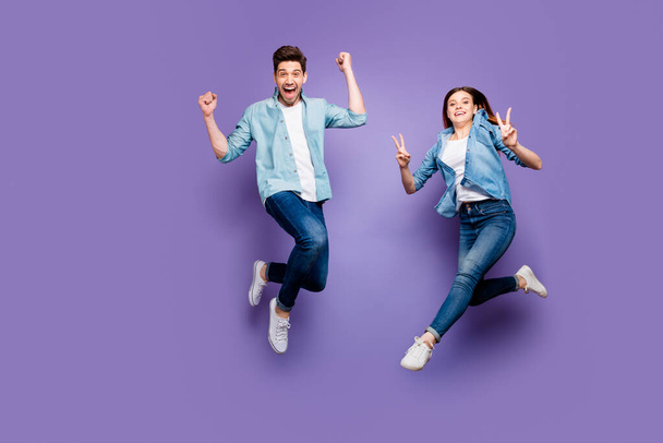 Full size photo of crazy cheerful brown hair redhair funny funky spouses jump have rest raise fists scream yeah make v-signs wear denim jeans modern outfit isolated violet purple color background - Фото, зображення