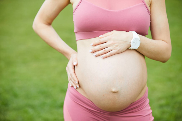 Lähikuva nuori raskaana oleva nainen vaaleanpunainen alkuun seisoo ulkona ja nauttia hyvästä säästä
 - Valokuva, kuva