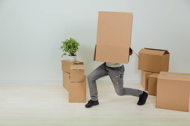 Funny man is standing with cardboard box on his head, hesitating, not seeing where to go. Handsome young man moving into new house. - Fotoğraf, Görsel