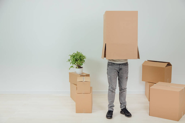 Funny man is standing with cardboard box on his head. Handsome young man moving into new house. - Φωτογραφία, εικόνα