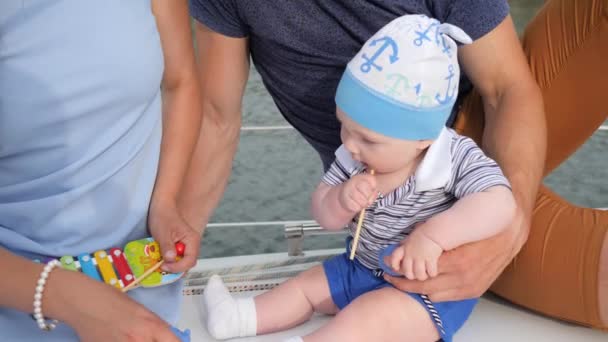 teething at baby which bites toys outdoors, good father with mother takes care of son on pleasure boat, - Footage, Video