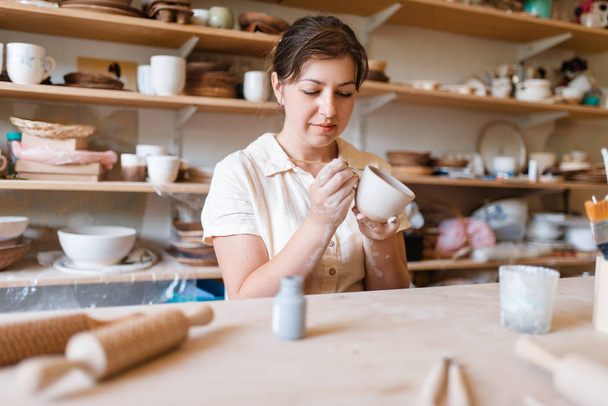 Female master paints a pot, pottery workshop. Woman molding a bowl. Handmade ceramic art, tableware from clay - Fotoğraf, Görsel