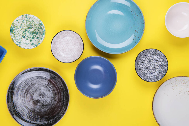 Set van kleurrijke moderne porseleinen borden en schalen op een gele achtergrond. designer keramiek in verschillende kleuren: blauw, turquoise, grijs en donkerblauw - Foto, afbeelding