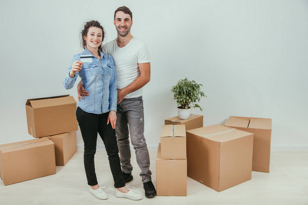 Husband is hugging his wife. Pretty wife is holding a credit card. They are smiling, surrounded by carton boxes. - Photo, image