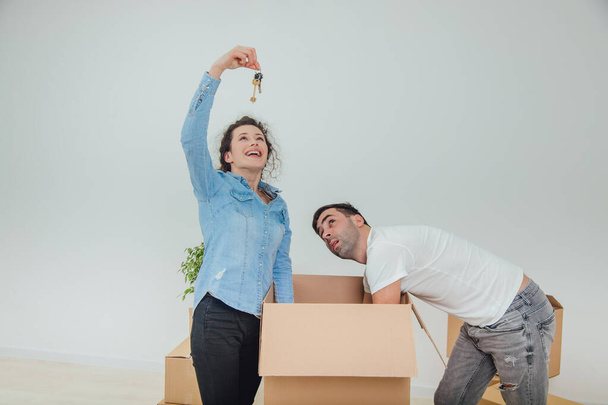Frau und Mann sind damit beschäftigt, die Kartons auszupacken. Frau steht, hält Schlüssel in der Hand, lächelt. - Foto, Bild