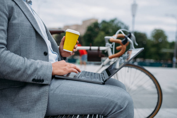 ダウンタウンのオフィスビルのベンチでサイクルドリンクコーヒーを飲むビジネスマン。街の通り、都市のスタイルでエコ輸送に乗るビジネス人 - 写真・画像