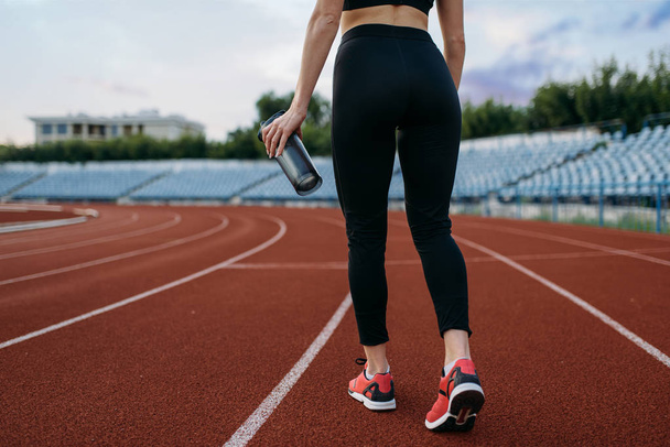 Běžkyně ve sportovním oblečení, pohled zezadu, trénink na stadionu. Žena dělá strečink cvičení před spuštěním na venkovní aréně - Fotografie, Obrázek