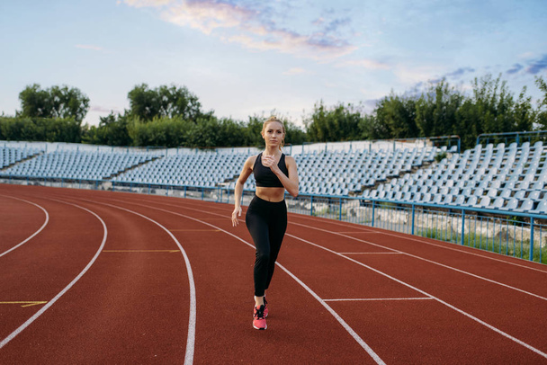 Běžkyně ve sportovním oblečení, trénink na stadionu. Žena dělá strečink cvičení před jogging na venkovní aréně - Fotografie, Obrázek