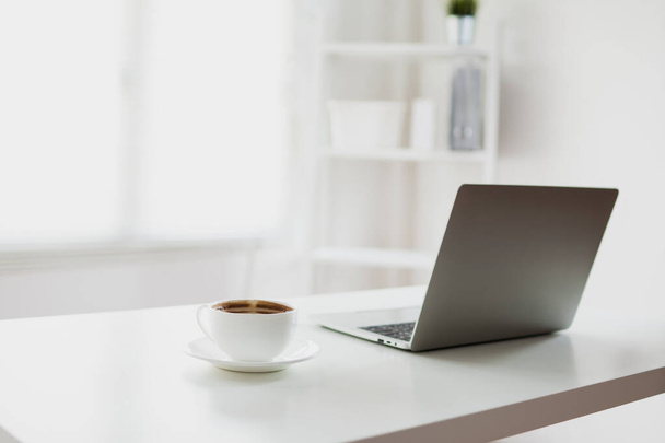 witte en heldere kantoorruimte met laptop en koffie op tafel  - Foto, afbeelding