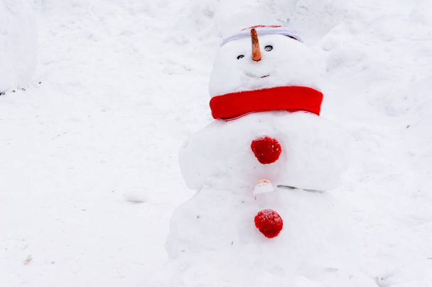 Kardan adam kış manzara beyaz kar yığınları nın arka planda duruyor. Çok kar var. Kırmızı şapkalı, atkılı ve düğmeli kardan adam. - Fotoğraf, Görsel