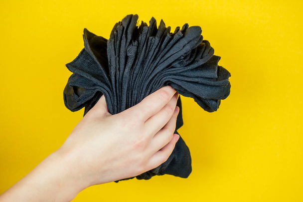 a stack of fresh new black socks in hand on a yellow background - Fotoğraf, Görsel
