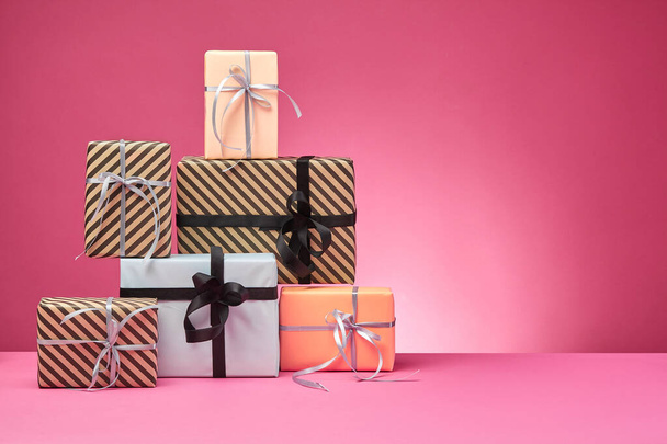 Different sizes, colorful, striped and plain paper gift boxes tied with ribbons and bows on a pink surface and background. Close-up, copy space. - Photo, Image