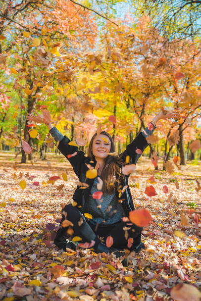 young pretty woman playing with yellow autumn leaves at city park - Photo, Image