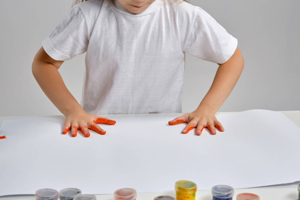 Pequeña artista de camiseta blanca de pie a la mesa con pinturas coloridas y hombre, pintando sobre ella con las manos. Isolado en blanco. Cierre. - Foto, Imagen