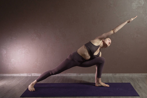Joven mujer atractiva deportista practicando yoga, meditando en pose de yoga, haciendo ejercicio, usando ropa deportiva, estudio de yoga marrón
 - Foto, Imagen