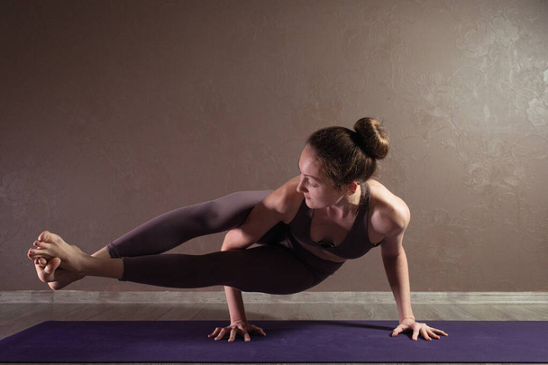 junge sportlich attraktive Frau praktiziert Yoga, meditiert in Yoga-Pose, trainiert, trägt Sportbekleidung, drinnen in voller Länge, braunes Yoga-Studio - Foto, Bild