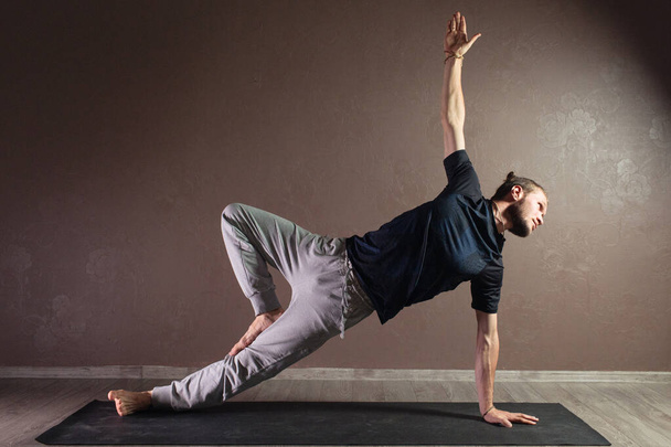 Nuori urheilullinen mies harjoittelee joogaa, meditoi Half Lotus poseeraa, treenaa, käyttää urheiluvaatteita, sisätiloissa täyspitkä, harmaa jooga studio
 - Valokuva, kuva