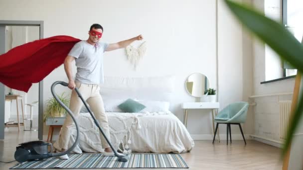 Portrait of smiling superman vacuuming carpet at home and looking at camera - Séquence, vidéo
