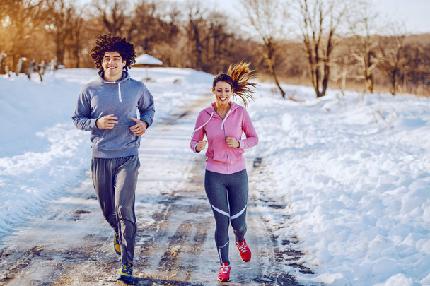 Happy smiling caucasian couple in sportswear running side by side in nature. Winter time. - Photo, Image