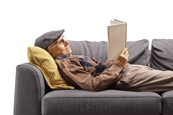 Elderly man lying on a couch and reading a book  - Фото, изображение
