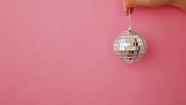 Simpelweg minimale ontwerp vrouw hand houden kerst ornament disco bal geïsoleerd op roze pastel kleurrijke trendy achtergrond - Video