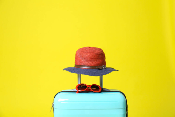 Stylish blue suitcase with hat and sunglasses on yellow background - Foto, Bild
