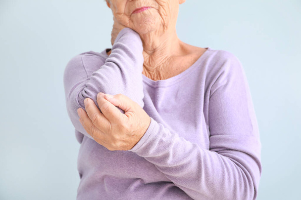 Ηλικιωμένη γυναίκα που υποφέρει από πόνο στον αγκώνα με φόντο το φως, κοντινό πλάνο - Φωτογραφία, εικόνα