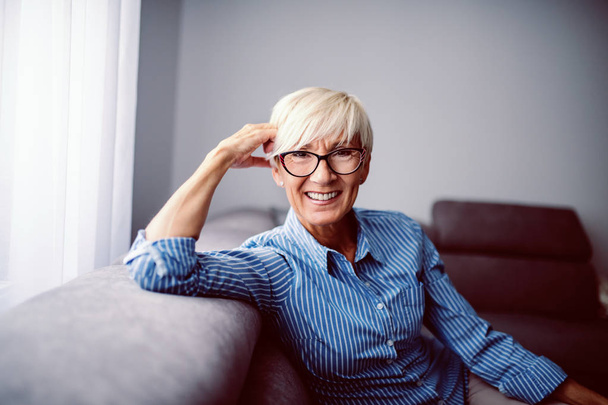 Gorgeous smiling senior woman dressed in striped shirt and with eyeglasses posing and looking at camera. - Photo, Image