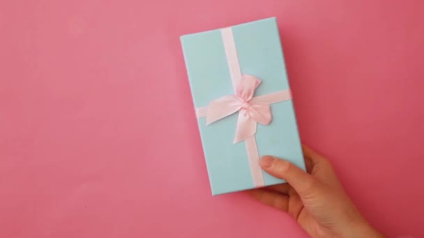 Yksinkertaisesti suunnitella nainen käsi tilalla sininen lahja laatikko eristetty vaaleanpunainen pastelli värikäs trendikäs tausta
 - Materiaali, video