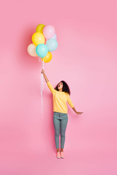 Vertical full body photo of cute nice girl with many baloons in hand feeling the wind become stronger and can be blown up to the sky isolated shiny color background - Foto, afbeelding