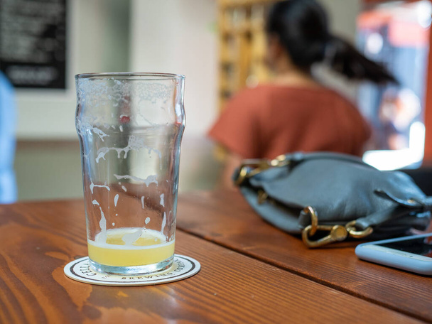 Terminado vaso de cerveza en la mesa al lado del bolso de la mujer y el teléfono
 - Foto, imagen