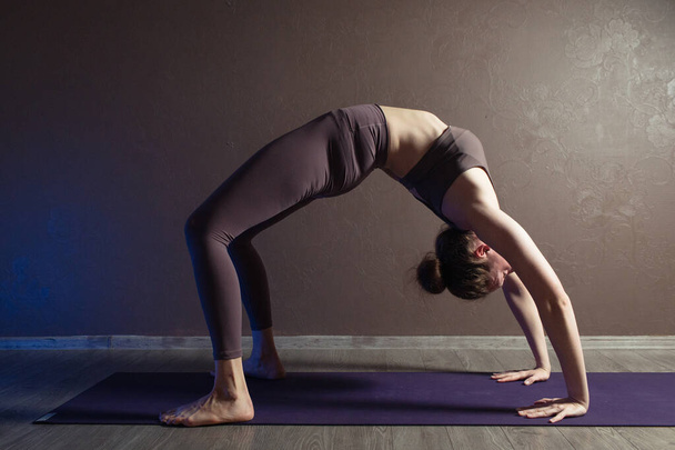 Jeune femme séduisante sportive pratiquant le yoga, méditant dans la pose de yoga, faisant de l'exercice, portant des vêtements de sport, intérieure pleine longueur, studio de yoga brun
 - Photo, image