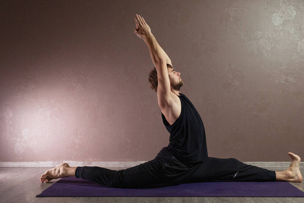 Jovem homem esportivo praticando ioga, meditando em pose de ioga, exercitando-se, vestindo roupas esportivas, comprimento total interior, estúdio de ioga marrom
 - Foto, Imagem