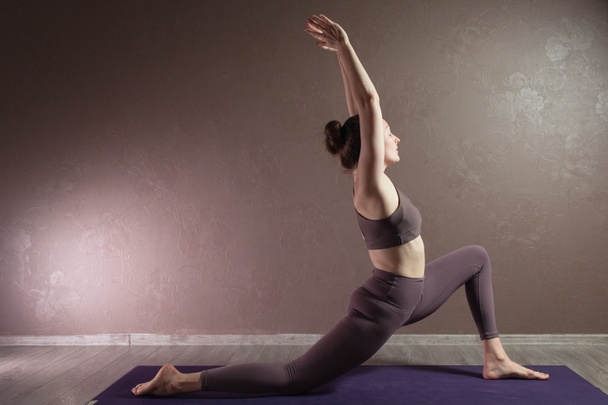 Młoda sportowa atrakcyjna kobieta ćwicząca jogę, medytująca w pozycji do jogi, ćwicząca, ubrana w odzież sportową, kryta pełna długość, brązowa pracownia jogi - Zdjęcie, obraz
