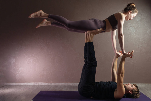 Молодой спортсмен и девушка практикуют йогу, медитируют в позе йоги, тренируются, носят спортивную одежду, крытая полная длина, студия коричневой йоги
 - Фото, изображение