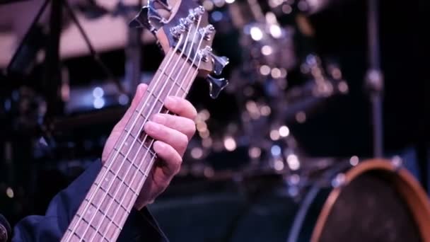  The musician's hand clamps the strings on a five-string electric bass. Close-up. Performance by an orchestra or a jazz band. Guitar player on the background of percussion instruments on stage. - Footage, Video