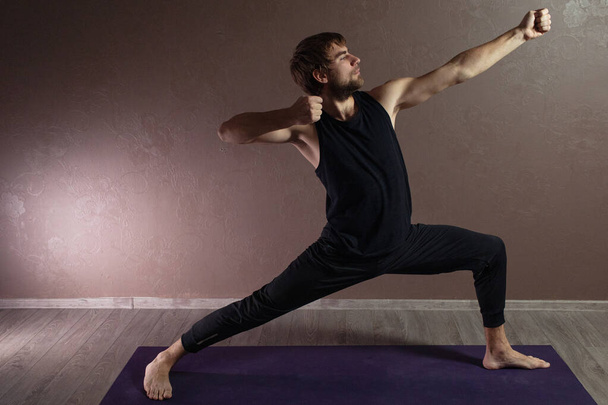 Молодой спортсмен практикующий йогу, медитирующий в позе йоги, тренирующийся, одетый в спортивную одежду, крытая полная длина, студия коричневой йоги
 - Фото, изображение
