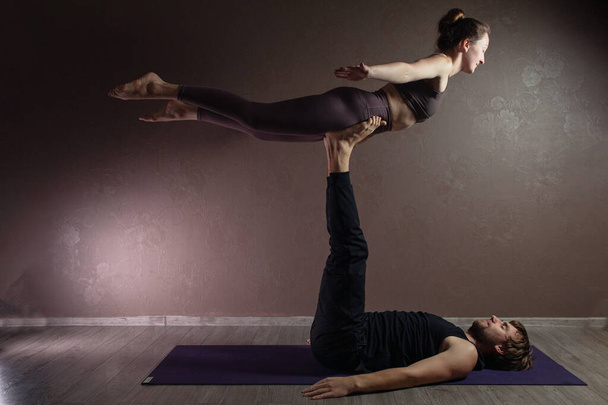 Genç sporcu erkek ve kız yoga yapıyor, yoga pozisyonunda meditasyon yapıyor spor kıyafetleri giyiyor, kapalı alanda yoga yapıyor, kahverengi yoga stüdyosu. - Fotoğraf, Görsel