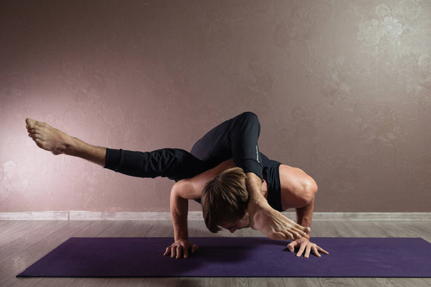 Young sporty man practicing yoga, meditating in Half Lotus pose, working out, wearing sportswear, indoor full length, brown yoga studio - Zdjęcie, obraz