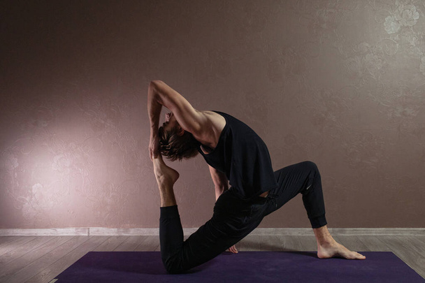 junger sportlicher Mann praktiziert Yoga, meditiert in Yoga-Pose, trainiert, trägt Sportbekleidung, drinnen in voller Länge, braunes Yoga-Studio - Foto, Bild