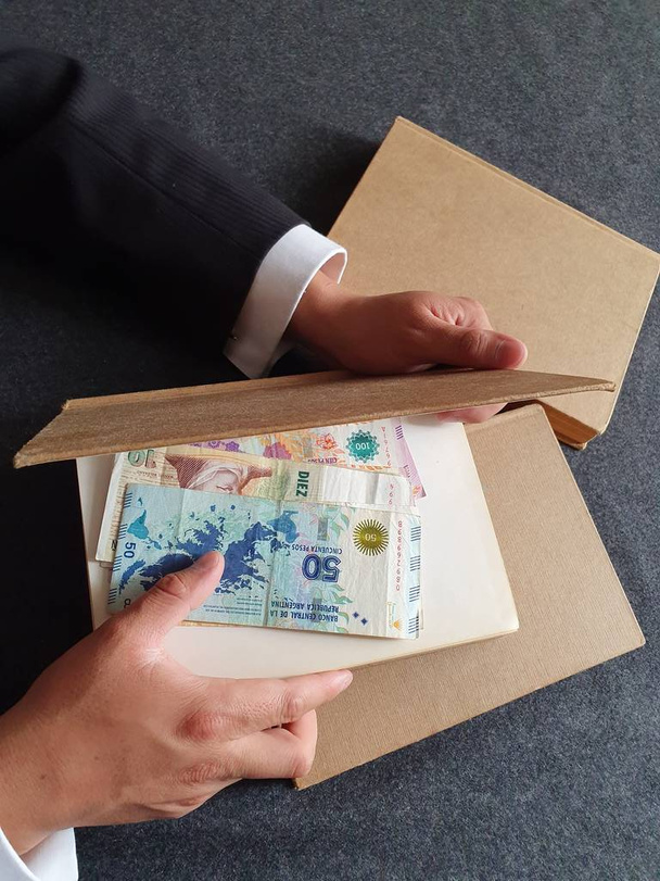 Hände eines Geschäftsmannes mit argentinischem Geld und Büchern auf dem Tisch  - Foto, Bild