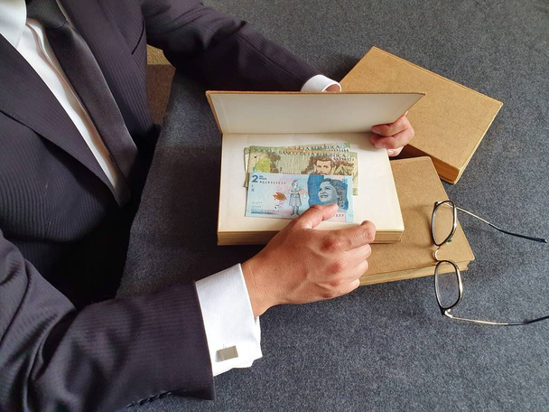 Hände eines Geschäftsmannes mit kolumbianischem Geld und Büchern auf dem Tisch  - Foto, Bild