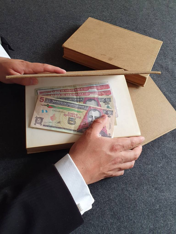Hände eines Geschäftsmannes mit guatemaltekischem Geld und Büchern auf dem Tisch  - Foto, Bild