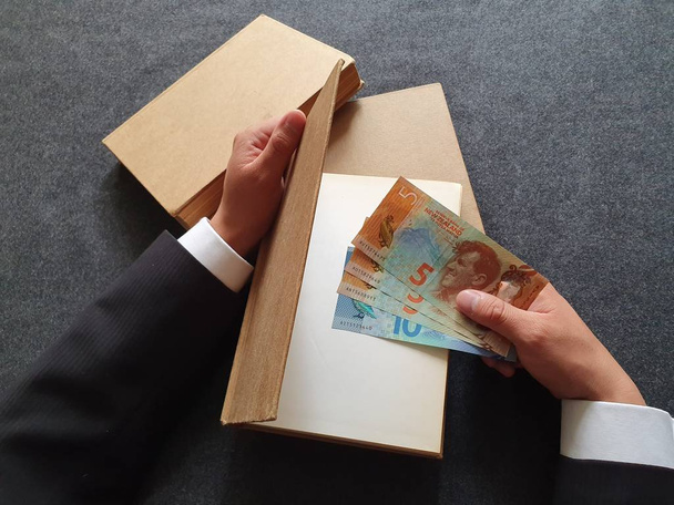 Hände eines Geschäftsmannes mit frischem Geld und Büchern auf dem Tisch  - Foto, Bild