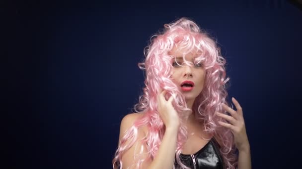 Χαριτωμένο κορίτσι με ροζ σγουρή περούκα σε μαύρο δερμάτινο κορσέ φλερτάρει κοιτάζοντας την κάμερα. περιπέτειες παράξενων ανθρώπων. - Πλάνα, βίντεο