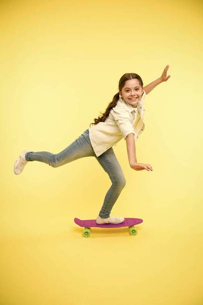 Kid having fun with penny board. Hobby favorite activity. Child smiling face stand on skateboard. Penny board cute colorful skateboard for girls. Lets ride. Girl ride penny board yellow background - Photo, image
